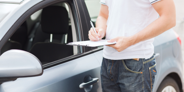 Image of person standing by a secondhand car with a clipboard, checking condition